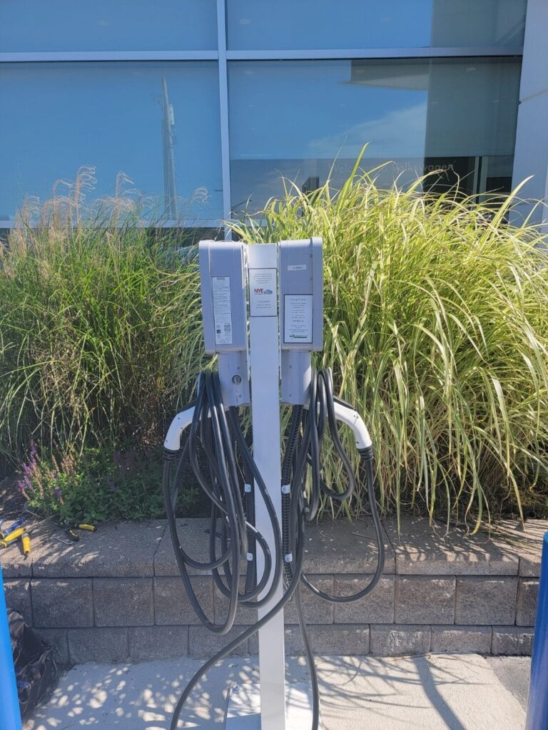 A close-up of a dual-port EV charging station installed outside a commercial building, surrounded by decorative landscaping.
