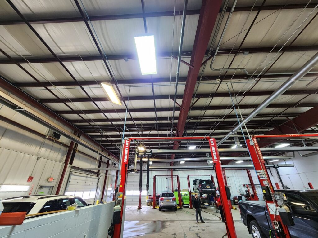 An automotive repair shop with older, dimmer lighting in the ceiling, showcasing the workspace before a lighting upgrade