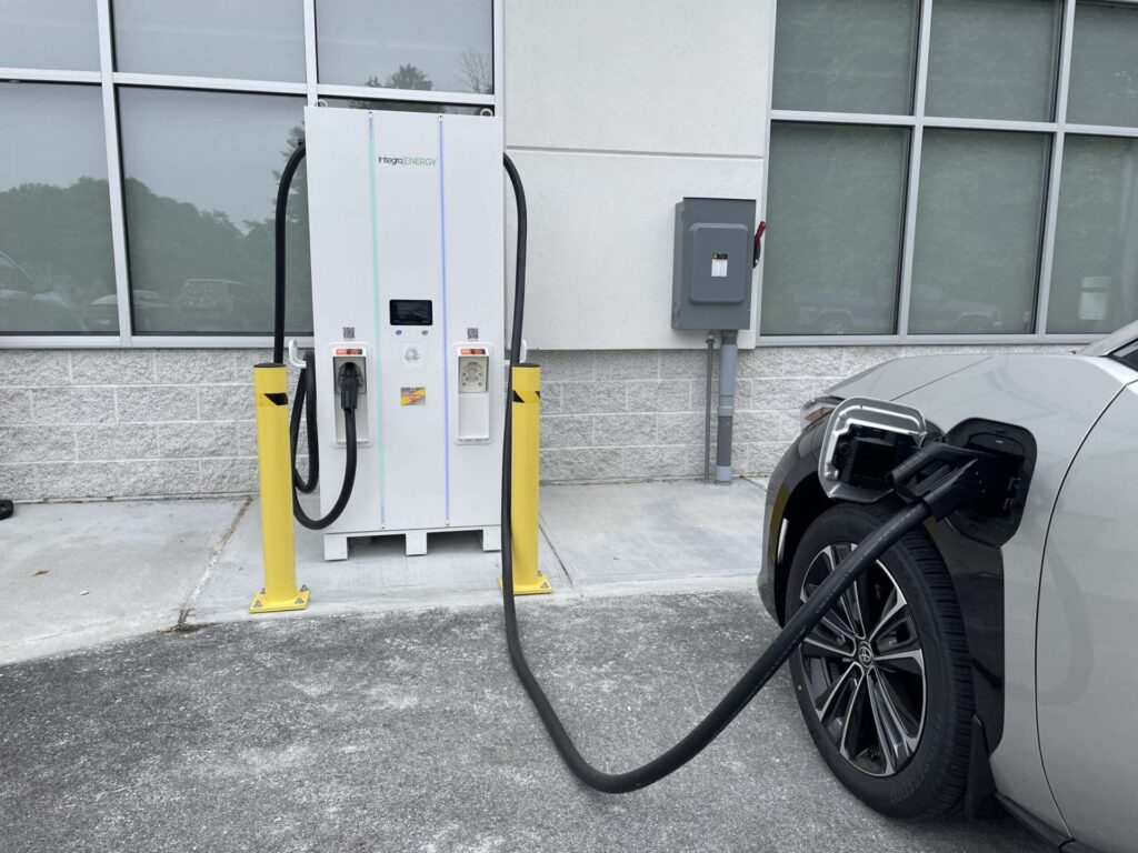 An Integra Energy electric vehicle charging station installed outside a commercial building, actively charging a gray EV parked nearby.
