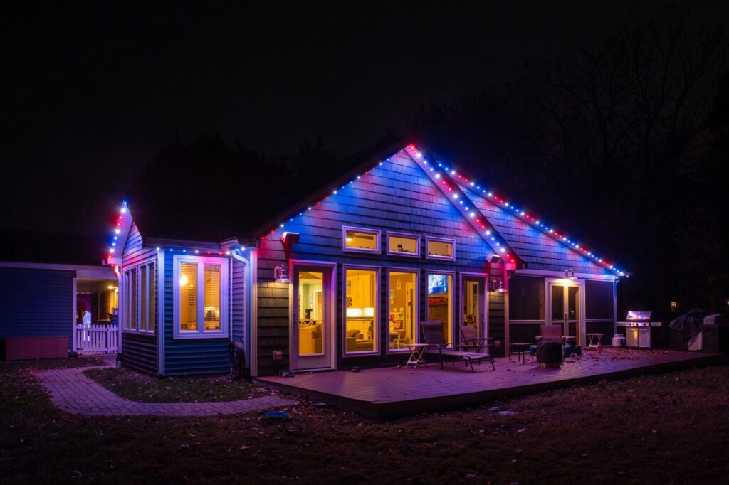 A house illuminated with Oelo permanent holiday lighting in red, white, and blue colors, showcasing a festive design. The lights are installed along the roofline, blending seamlessly with the house exterior at night another angle