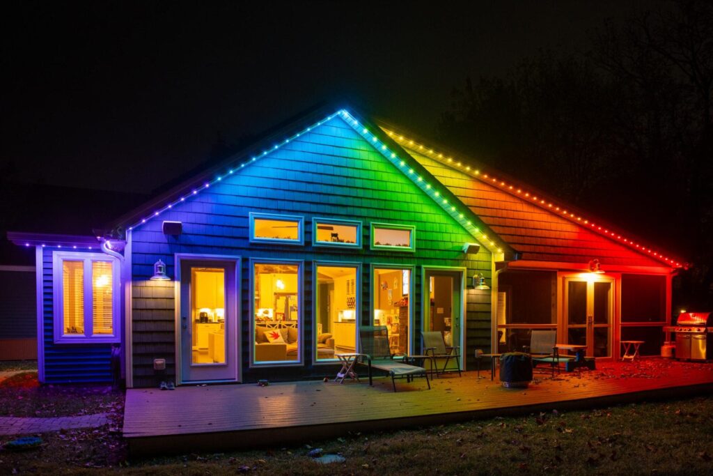A house illuminated with Oelo permanent holiday lighting in rainbow colors, showcasing a festive design. The lights are installed along the roofline, blending seamlessly with the house exterior at night