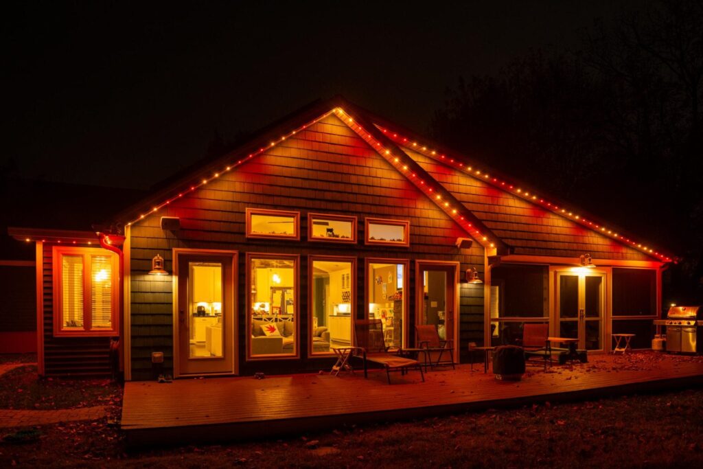 A house illuminated with Oelo permanent holiday lighting in red and orange colors, showcasing a festive design. The lights are installed along the roofline, blending seamlessly with the house exterior at night