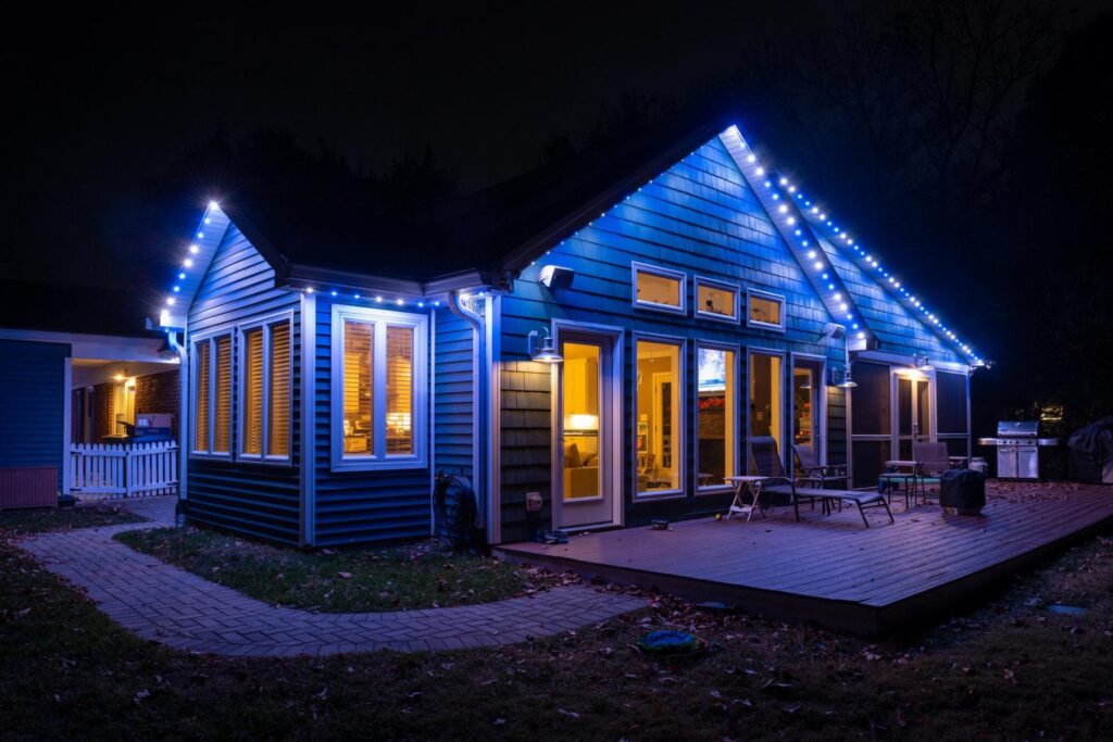 A house illuminated with Oelo permanent holiday lighting in white, and blue colors, showcasing a festive design. The lights are installed along the roofline, blending seamlessly with the house exterior at night another angle