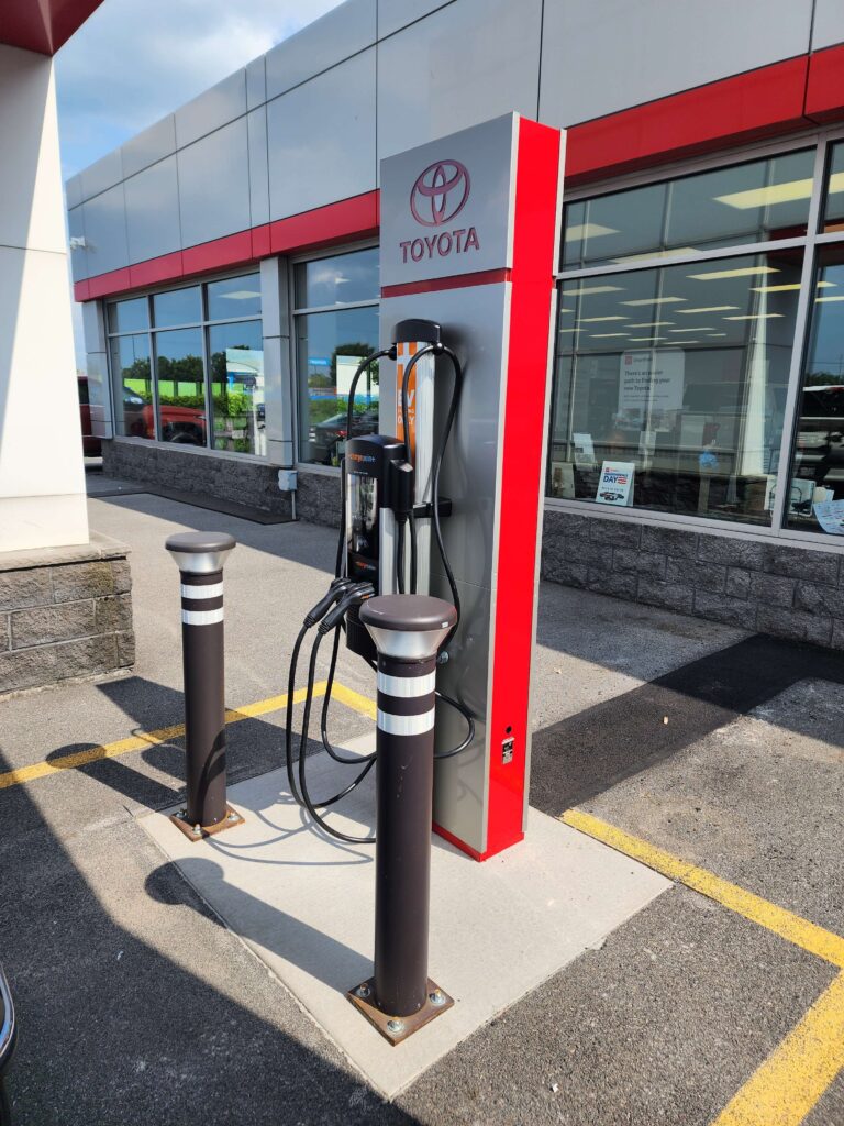 Electric vehicle charging station installed at a Toyota dealership parking lot, featuring a ChargePoint Level 2 EV charger with protective bollards and branded Toyota signage.