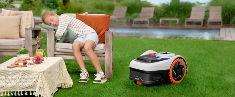 Quiet robotic lawn mower operating on a green backyard lawn while a child naps peacefully on an outdoor chair nearby, illustrating ultra-quiet mowing performance that does not disturb family or relaxation in a residential garden setting.