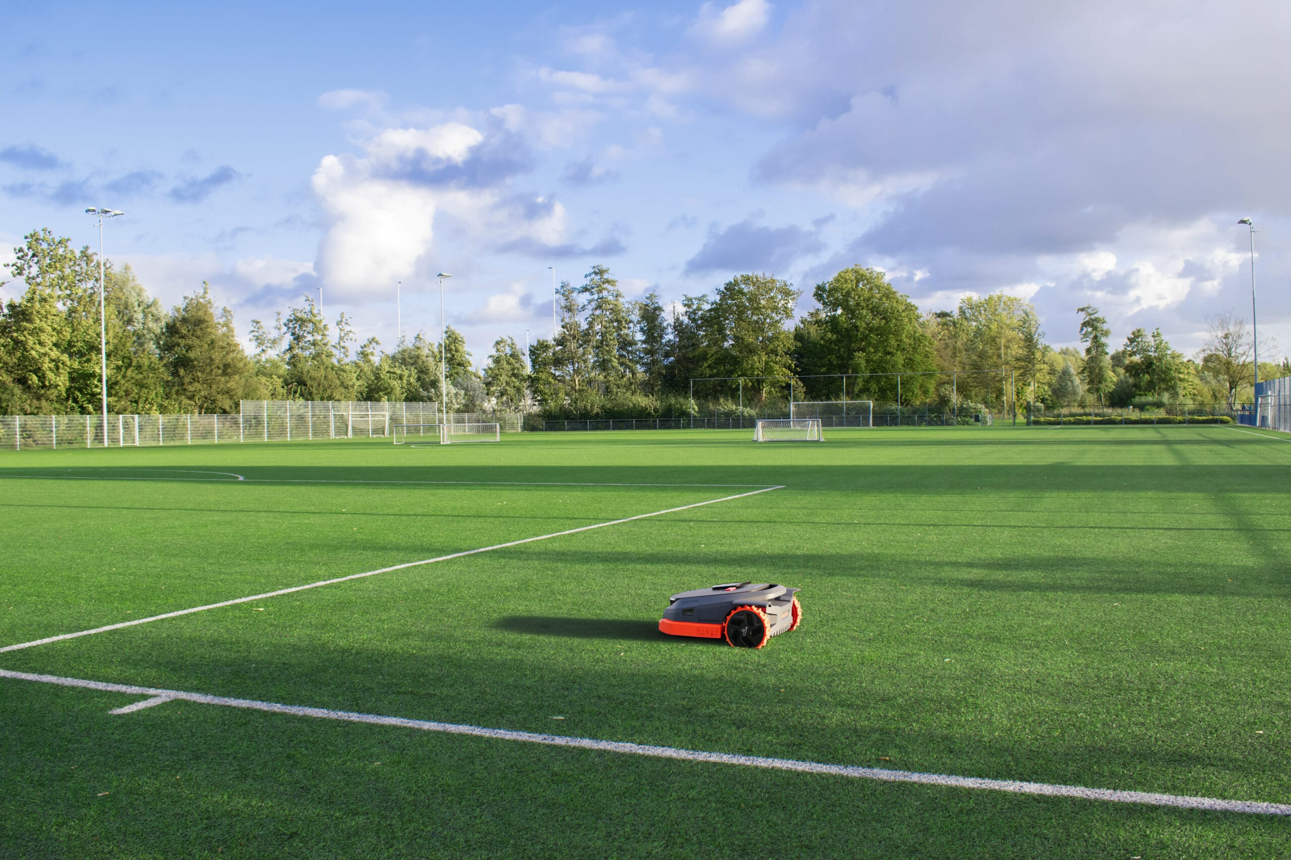 Segway Navimow robotic lawn mower operating on a large, well-maintained sports field under a partly cloudy sky