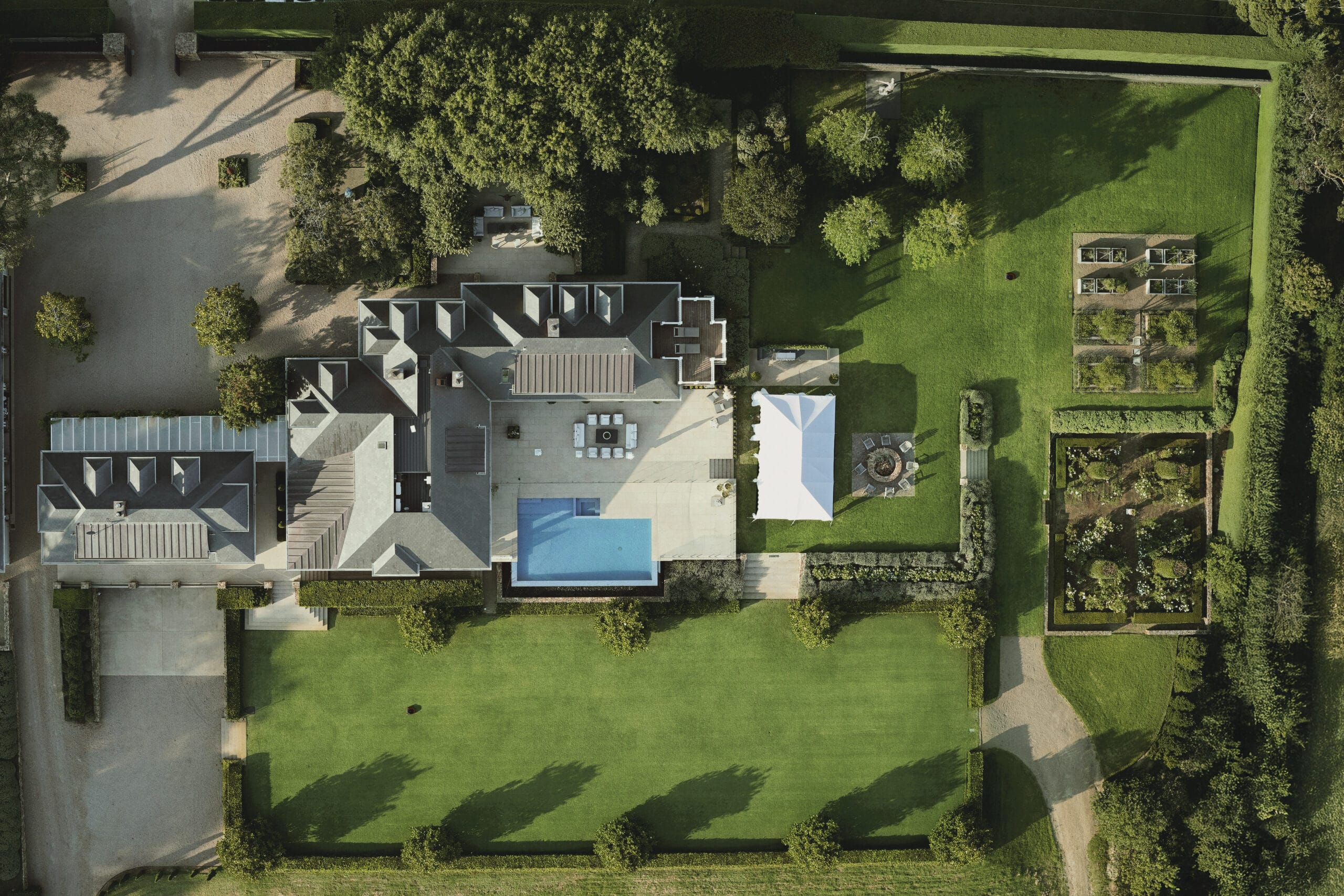 Aerial view of a modern property with landscaped lawns, gardens, and a Segway Navimow robotic mower in operation.