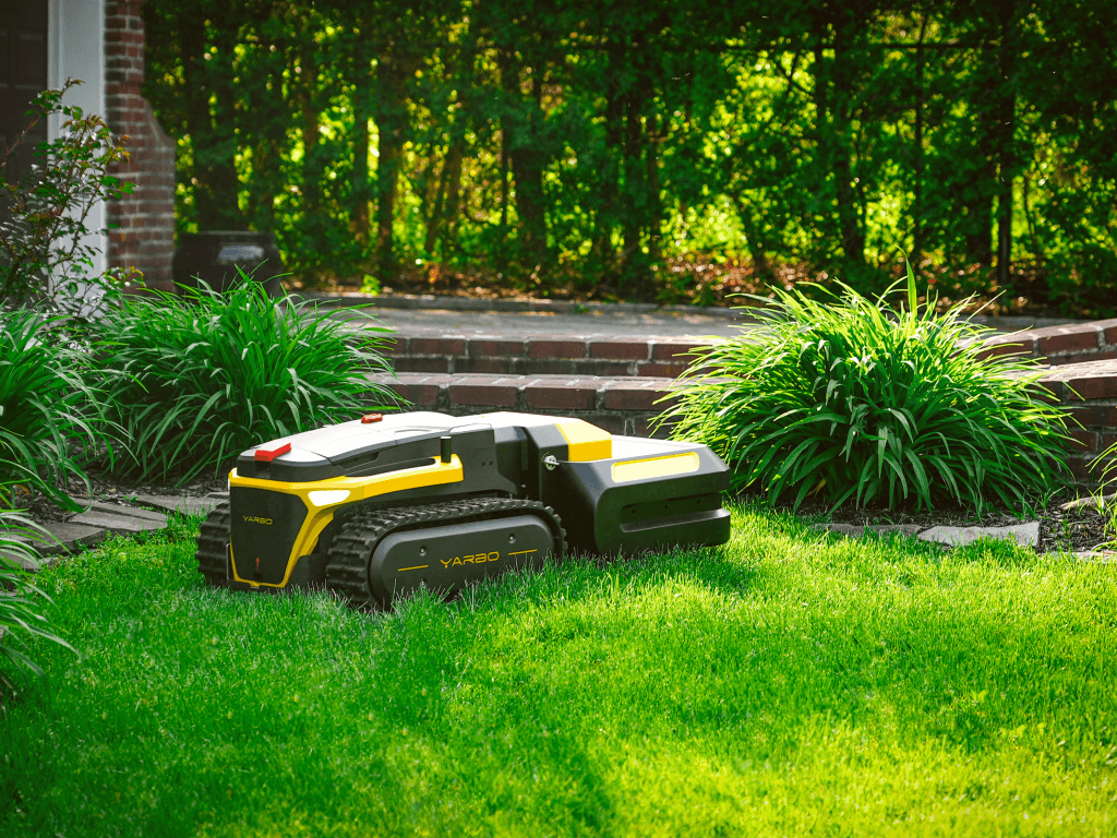 Yarbo Pro Mower cutting grass in a landscaped backyard with brick steps and garden plants.