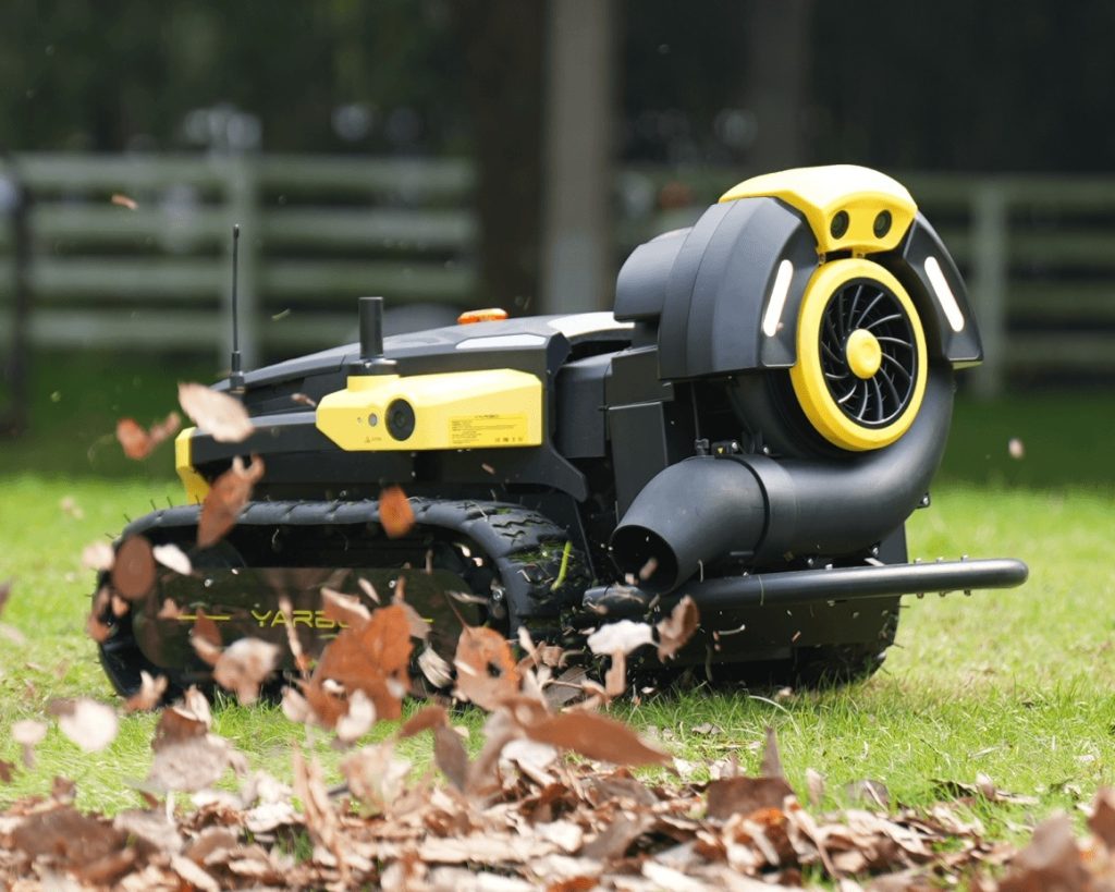 Yarbo robot operating with the Leaf Blower Module attached, blowing leaves and debris across a grass lawn.