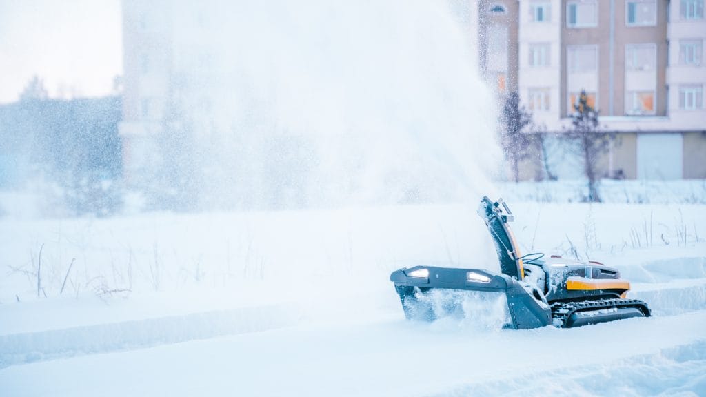 Yarbo robotic snow blower clearing deep snow and throwing a large plume of snow into the air in a residential winter setting.
